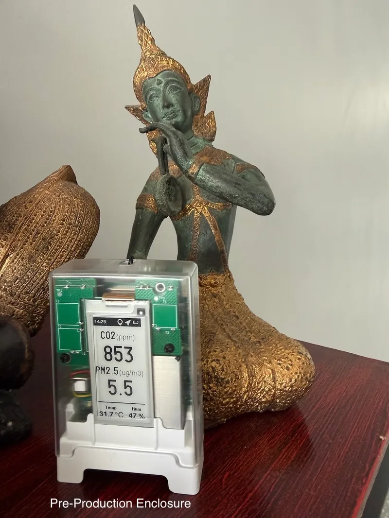 Portable air quality monitor on a table beside a Thai-style statue